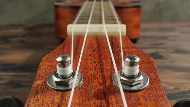 Close up camera movement over wooden ukulele fretboard and tuning pegs of traditional four string musical instrument.