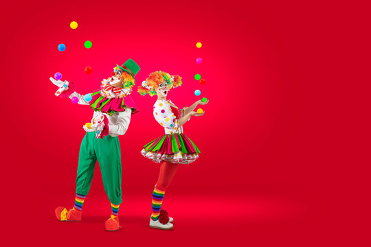Surprised juggler clowns juggling balls in the circus, woman entertainer as Joker in suit and wig, with clown whiteface makeup. Trickster, jester, pantomime, mime,  professional actor at events