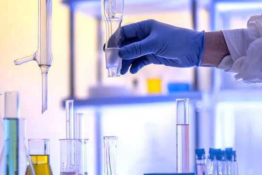 Close up of a gloved hand holding a glass rectification fractionating column among laboratory glassware. Concept for distillation, chemical engineering and analytical chemistry, copy space.