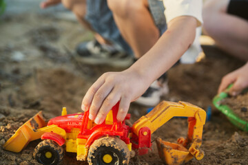 The hand of a boy child moves an excavator toy with large wheels in the sandbox. Red Plastic Toy With Ladle. High quality photo © Rystemys