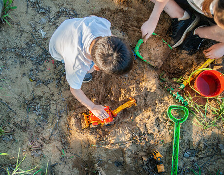 Children playing in the sandbox. Under the evening sun, a child plays in a sandbox with a toy plastic red excavator. Close-up photo without a face, focus on an excavator toy car. High quality photo