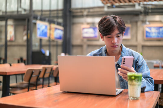 Asian man using phone with laptop