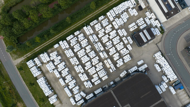 Purmerend, North Holland, Netherlands - 15 June 2026: Aerial view of a storage lot filled with white caravans and trailers parked in neat rows next to a warehouse and canal.