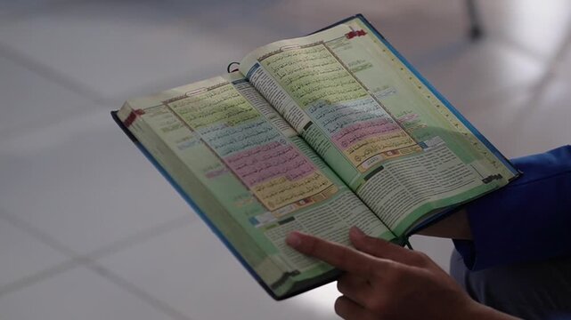 Close-up footage of an open Quran being read during an Islamic study or prayer session. The scene focuses on the sacred text while hands are respectfully folded nearby, creating a peaceful and spiritu