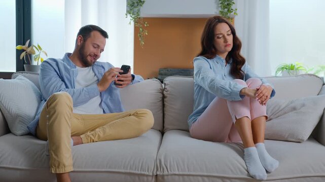 Offended jealous Caucasian woman looking at man with suspicion distrust husband chatting with mobile phone gadget addicted texting messaging with smartphone ignoring wife. family crisis at home