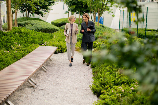 Business professionals walk in a garden pathway discussing ideas during a work meeting