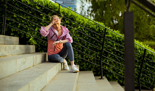 Woman resting on steps after workout near greenery on a sunny day