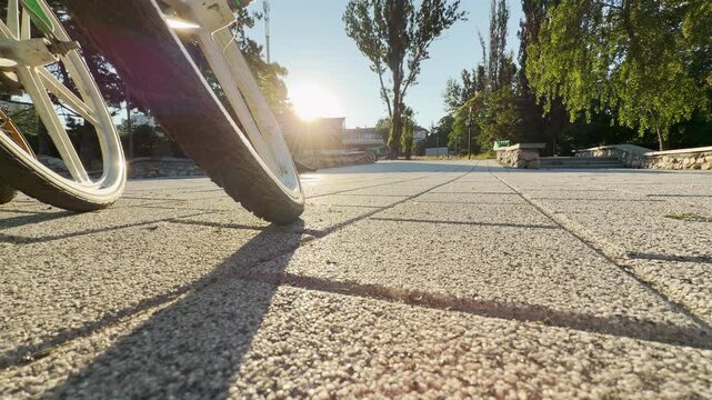 Parked bicycle wheels rest on a stone path in Simferopol, Crimea. The bright morning sunrise brings a hopeful feeling as warm shadows stretch across the park walkway.