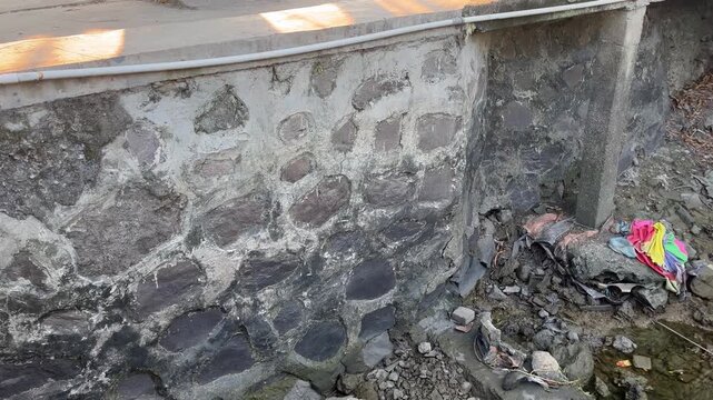 Cracked stone retaining wall and collapsed drainage infrastructure