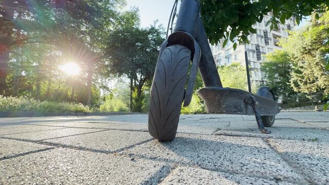An electric scooter stands on a paved path in Simferopol, Crimea. Intense morning sunburst shines through the park trees, creating a warm, energetic, and hopeful feeling.