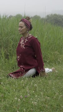 Mature woman doing yoga pigeon pose in a meadow