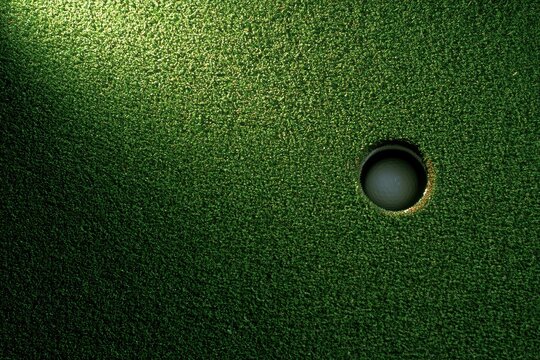 Close-up abstract of a putting green with a golf hole and dramatic light