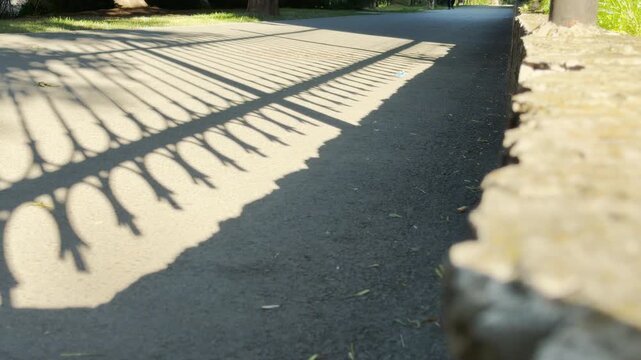 Intricate fence shadows cover a quiet walkway in Simferopol, Crimea. This peaceful scene brings a feeling of nostalgic warmth and gentle serenity. The bright summer day feels calm.