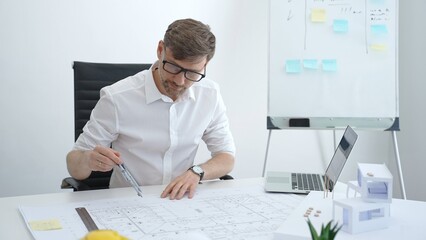 Naklejka premium Male architect drawing on building blueprints with a compass, developing architectural plans for a new house model, and working on construction design in a modern office