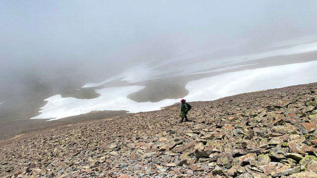 Mountain trekker descends through rugged terrain near Didi Abuli in Georgia with melting snowfields, low clouds and remote wilderness, wide view, hiking adventure concept.