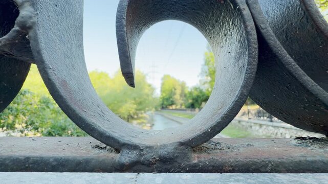 A close-up metal scroll frames a blurry park and river in Simferopol, Crimea. This unique view brings a curious and peaceful feeling of calm nostalgia.