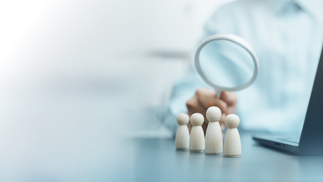 HR professional using a magnifying glass to evaluate candidates represented by wooden figures, illustrating recruitment, talent acquisition, employee screening, and workforce selection.