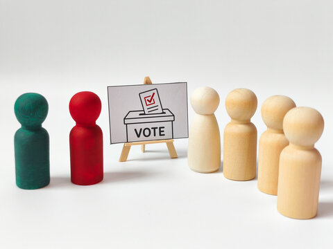 Democracy and corporate voting concept with wooden peg doll candidates and voters standing by a ballot box.