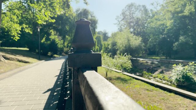 A metal railing lines a paved path in a sunlit park in Simferopol, Crimea. The bright, warm sunshine creates a deeply peaceful and joyful feeling.