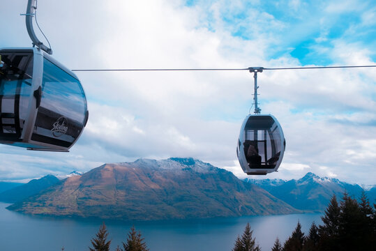 Queenstown, New Zealand: Skyline Gondola cabins suspend over Lake Wakatipu and dramatic Cecil Peak alpine mountain landscape travel background.