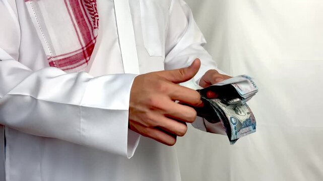 Saudi man wearing traditional thobe counting five hundred riyal banknotes close up.