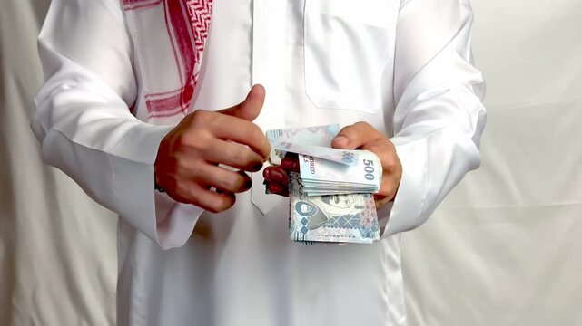 Saudi man wearing traditional thobe counting five hundred riyal banknotes close up.