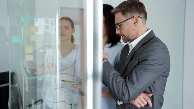 Business team collaborating on strategy, brainstorming ideas with post it notes on a glass board during an office meeting, planning effective project development