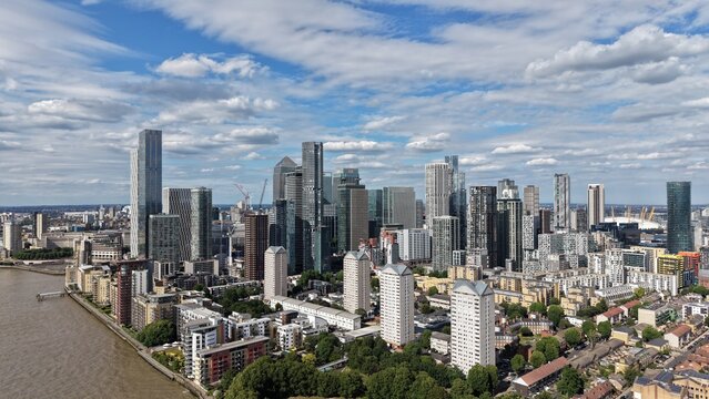 London, United Kingdom - 16 June 2026: Aerial view of the modern skyscrapers of Canary Wharf financial district with residential blocks and the River Thames under a cloudy sky.