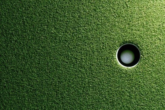 Close-up of a golf ball resting inside a putting green hole, illuminated