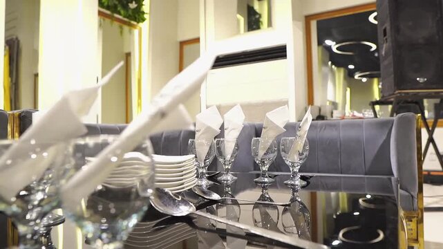Beautiful wedding reception table setup featuring crystal glassware, neatly folded napkins, stacked plates, cutlery, and elegant seating in a luxurious banquet hall. Ideal for wedding, hospitality, 