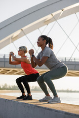 Naklejka premium Fit women doing squats while working out outdoors by the river
