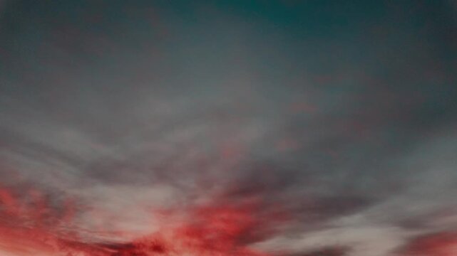 Dramatic 4K footage of vivid red glowing clouds against dark teal sky at sunset. Moody cinematic cloudscape, perfect background or overlay. timelapse