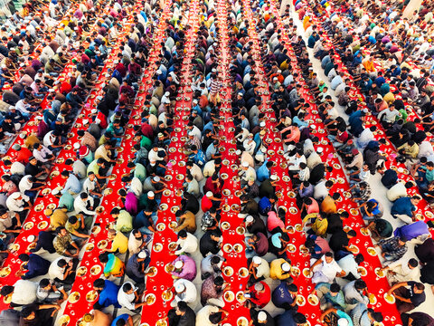 Dhaka, Bangladesh - 16 June 2026: Aerial view of a large crowd of people sitting in long rows on the floor during a mass community meal with red table runners and plates.