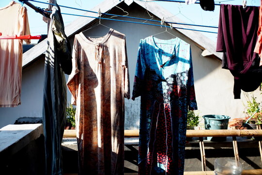 A vibrant outdoor shot of traditional Indonesian women's house dresses (daster), including one with batik pattern, hanging on a blue clothesline using hangers. on clothesline to dry outdoors