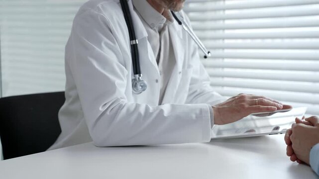 Doctor consulting patient, explaining treatment options and medical information using a digital tablet during a healthcare visit in a modern clinic setting