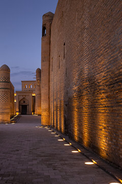 Ichan Kala old town illuminated at twilight in Khiva, Uzbekistan, with warm uplights along ancient brick walls. Ideal for travel publications, heritage brochures, and cultural tourism marketing.