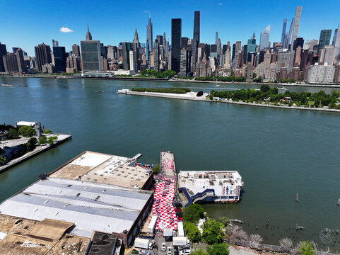 Long Island City, United States - 13 June 2026: Aerial view of a large red and white checkered banner on a pier along the East River with the Manhattan skyline in the background.