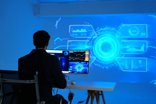 male programmer (professional) sits watching stock charts and computer-generated analysis of management systems, business intelligence, data statistics, and marketing analysis on a large monitor for i