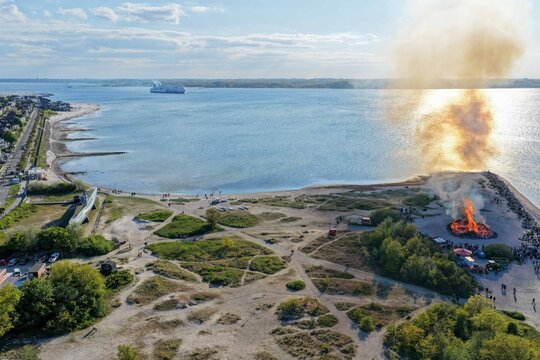 Laboe, Germany - 09 May 2026: Aerial view of the Maifeuer bonfire burning on the beach with smoke rising, the U-995 submarine monument, and a ferry on the Kiel Fjord.