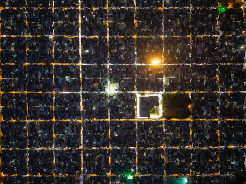 Aerial view of the dense urban grid of Malvani at night, featuring illuminated streets forming a geometric pattern between residential rooftops in Mumbai, Maharashtra, India.