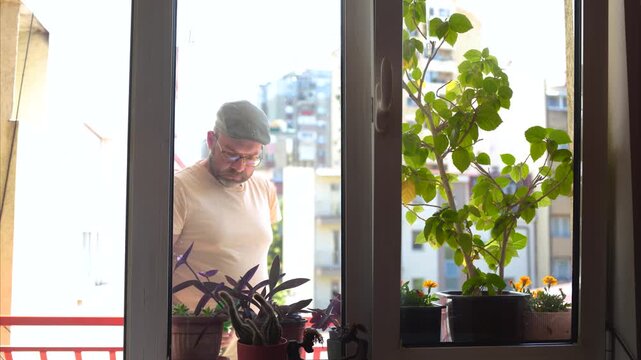Handsome hipster man watering flowers on a terrace window