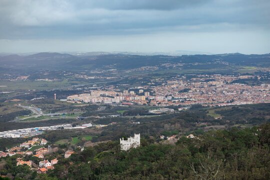 Vast rolling hills cradle a captivating urban enclave adorned with enchanting castles amid a backdrop of dramatic skies, showcasing the blending of nature and architecture