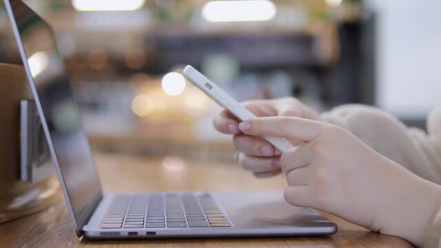 Close-up of hands scrolling phone beside laptop. Person focused, calm, engaged with digital devices. Suitable for tech, remote work, or digital lifestyle themes