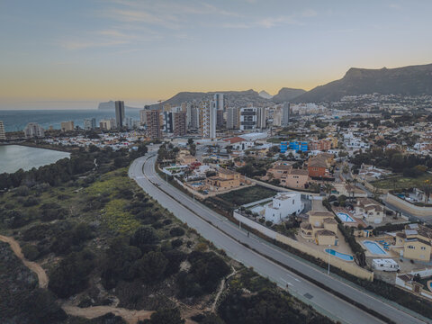 Aerial view of high-rise buildings, residential villas with swimming pools, and a winding road near the Mediterranean Sea in Calp, Valencian Community, Spain.