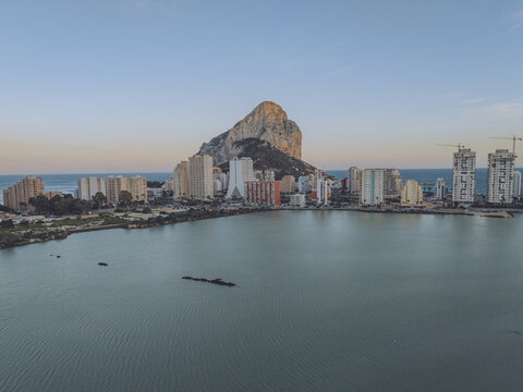 Aerial view of the iconic Penon de Ifach rising above the coastal town with modern apartment buildings and the Mediterranean Sea in Calp, Valencian Community, Spain.