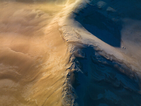 Aerial view of the sand dunes at Two Peoples Bay Nature Reserve, showing the contrast between golden sunlit slopes and deep blue shadows in Nanarup, Western Australia, Australia.
