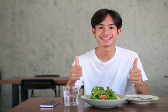 Young Asian non-binary man showing two thumbs up gestures at restaurant