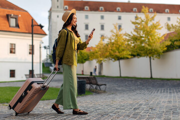 Woman walking with suitcase, looking at her cellphone in city, free space © Home-stock