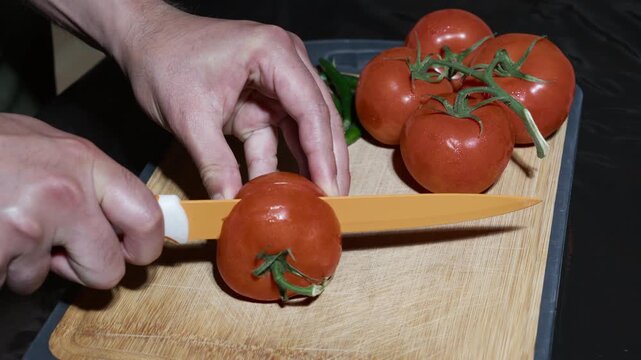 Food preparation concept as a man cuts ripe vine tomatoes on a chopping board with green chilies.