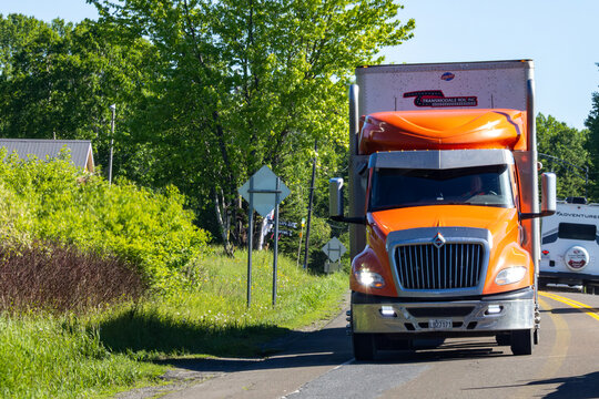 Gaspesie, Canada, 17 June 2026 : An orange International semi-truck from Transmodale RDL Inc. drives on a tree-lined road.